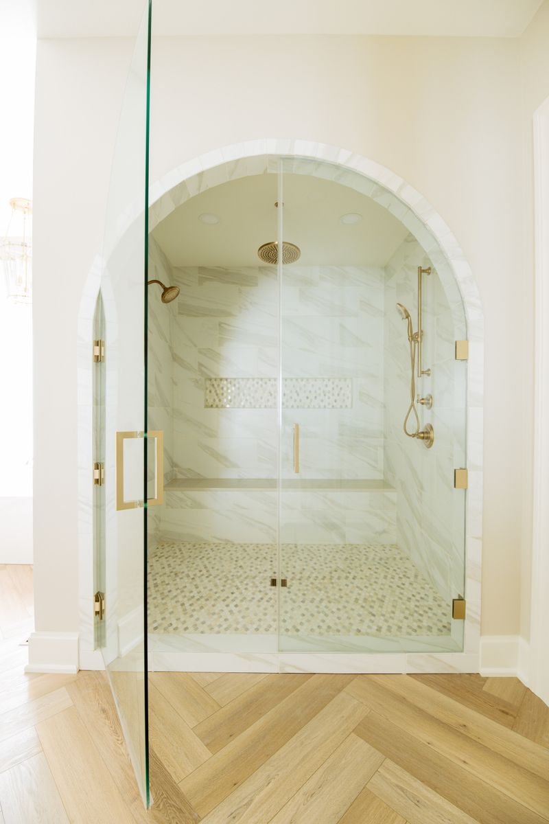 A primary bath in Urbandale with an arched marble tile shower and brass fixtures behind glass doors.