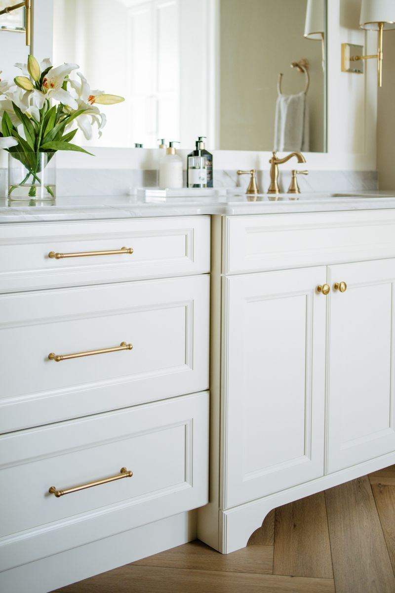 A primary bath in Urbandale with brass hardware on a white vanity under a marble countertop.