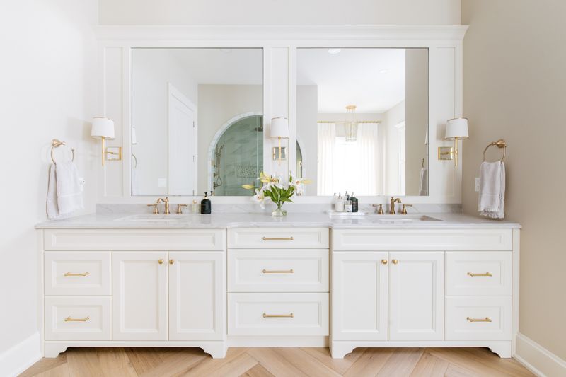 A primary bath in Urbandale with brass hardware on a cream vanity under a marble counter, over herringbone oak floors.