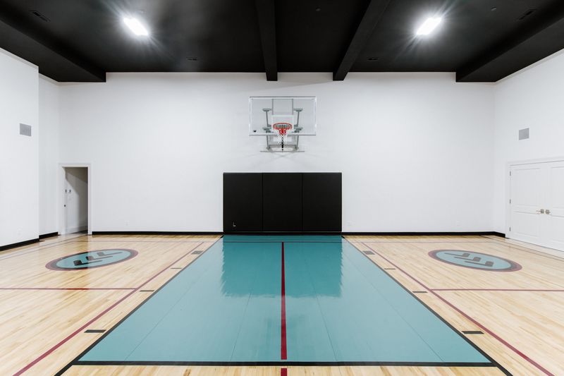 An indoor sport court in Urbandale with a teal painted key on maple floors under a black ceiling.