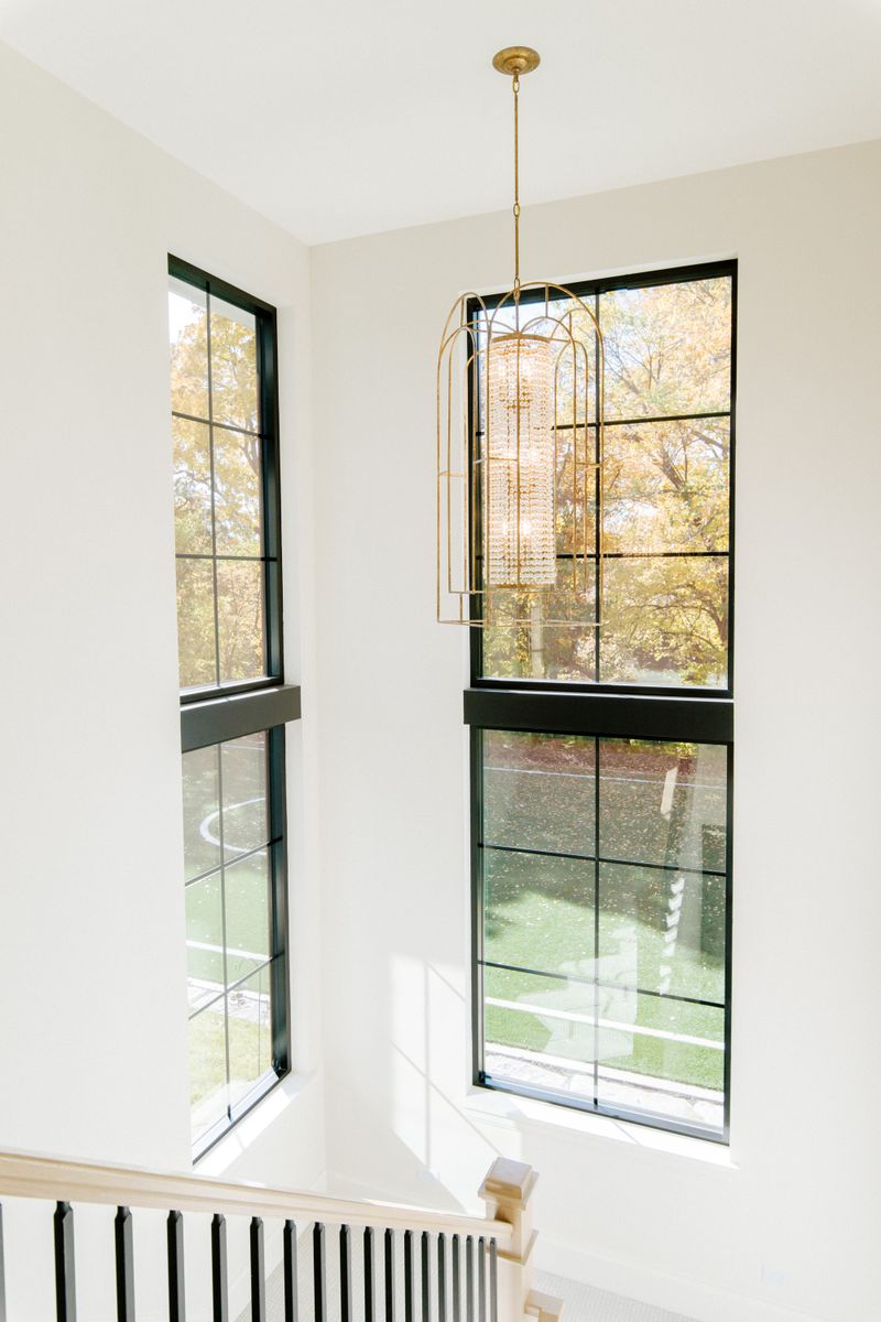 A stair landing in Urbandale with a gold crystal lantern hanging between tall black grid windows.