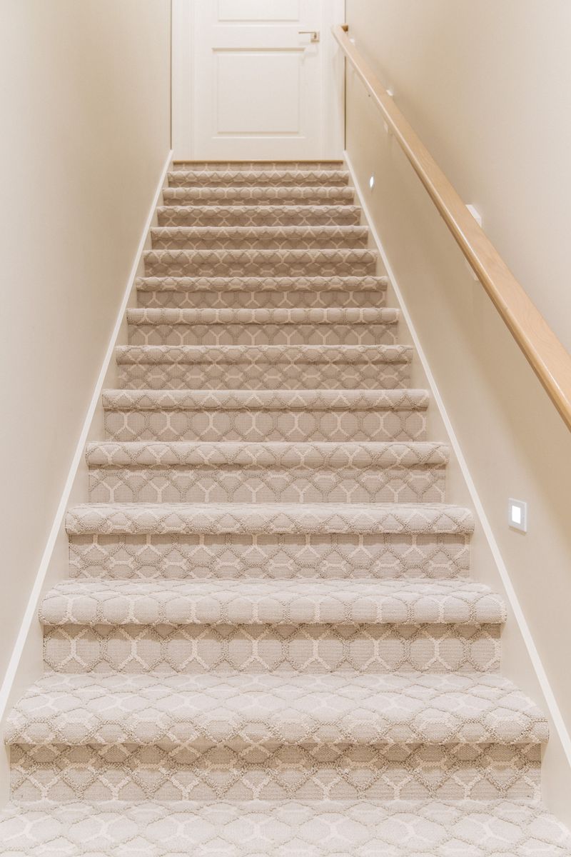 A staircase in Urbandale with a patterned cream carpet running the full width beside a white oak handrail.