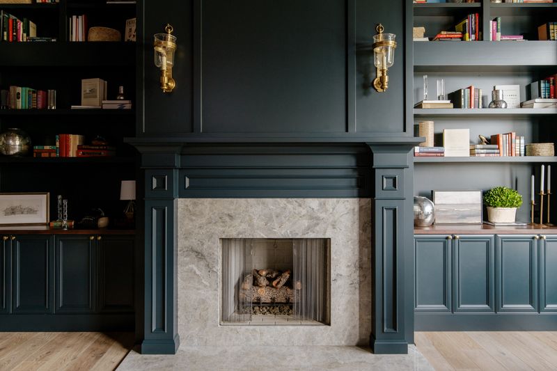 A study in Urbandale with dark green built-in shelves beside a fireplace framed in pale grey stone.