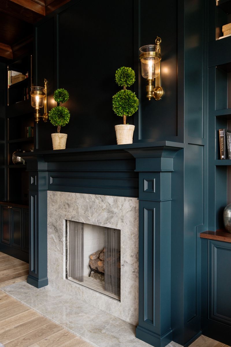 A dark teal study in Urbandale with a pale grey marble fireplace surround set into painted built-ins.