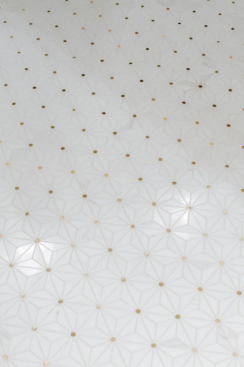 White marble star mosaic tile in Urbandale with small brass dots set at every point of the pattern.