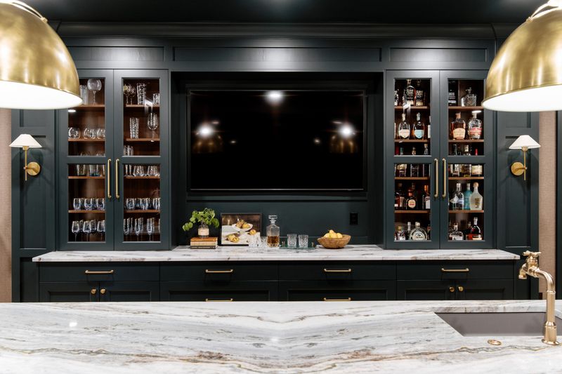 A dark green wet bar in Urbandale with glass front liquor cabinets above veined marble counters.