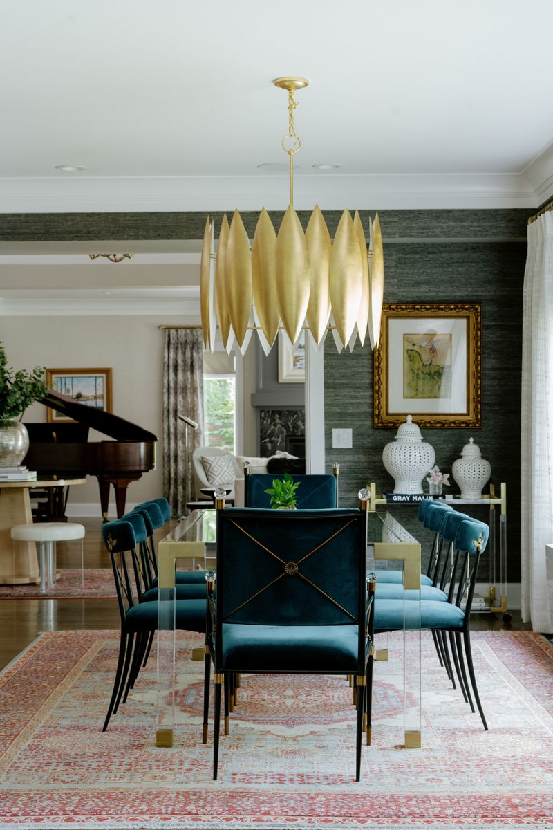 A dining room in Des Moines with a gold petal chandelier over teal velvet chairs and dark grasscloth walls.