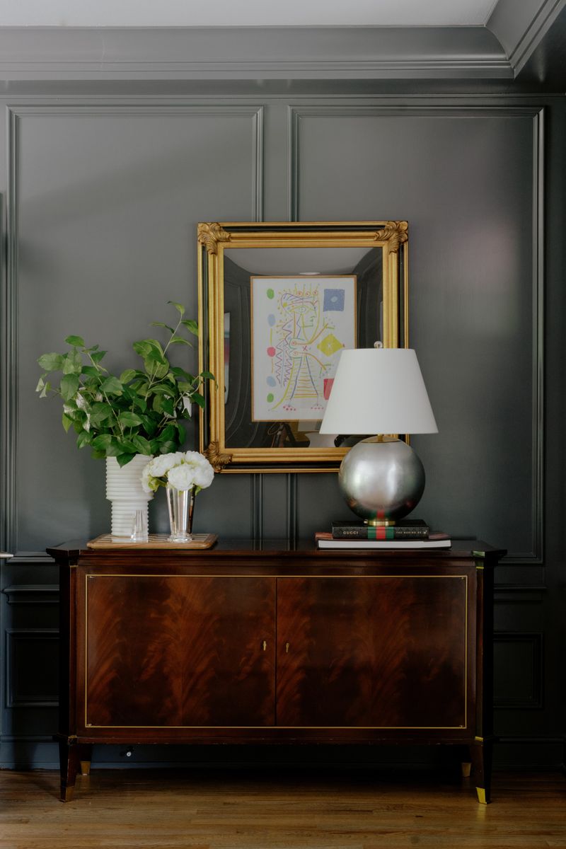 A dark green paneled entry in Des Moines with a gold framed mirror above a mahogany cabinet.