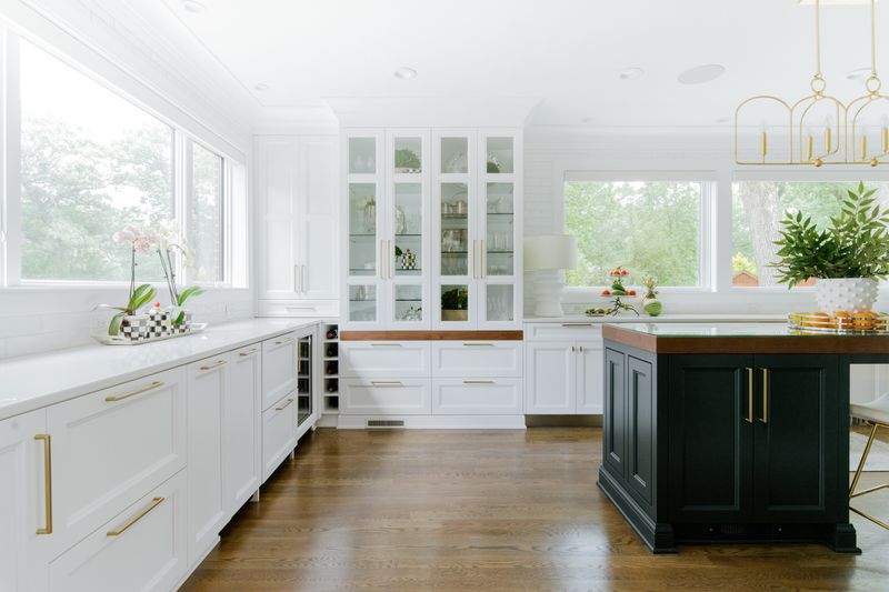 A white kitchen in Des Moines with a black island topped in butcher block wood and brass pulls.