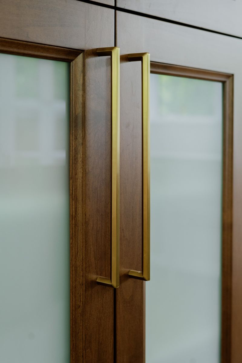 Long brass pulls on frosted glass kitchen cabinet doors in Des Moines, set in warm stained wood.