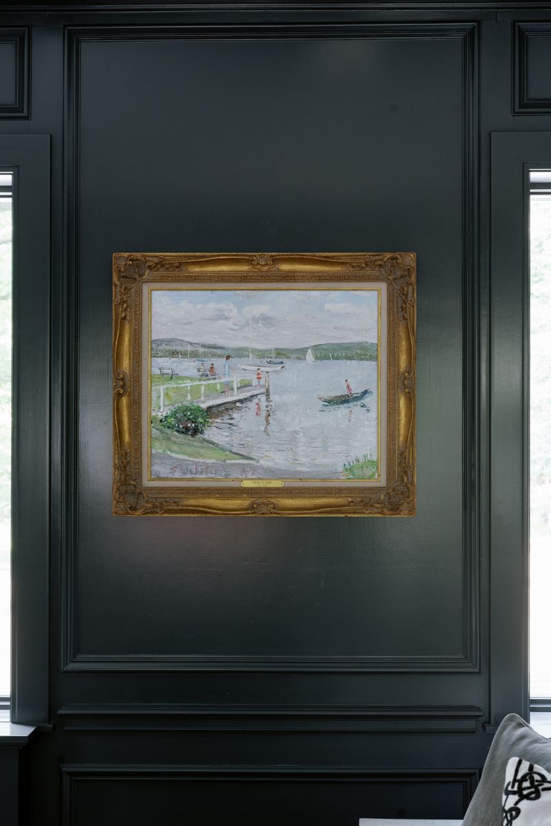 A dark green paneled wall in Des Moines with a gold framed harbor painting hung between two windows.