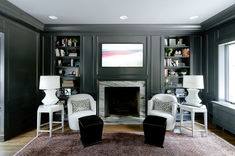 A charcoal paneled study in Des Moines with a marble fireplace between styled built-in shelves and two white boucle chairs.