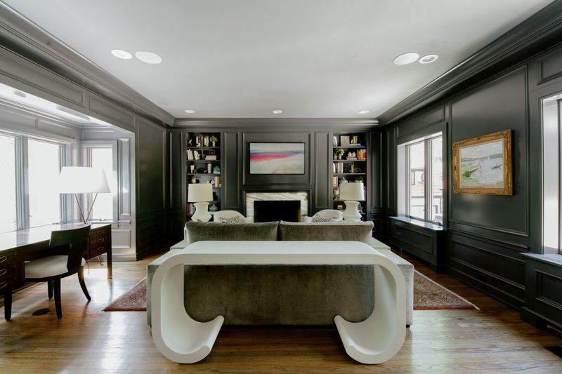 A private office in Des Moines with moody paneled walls and a curved white plaster coffee table on oak floors.