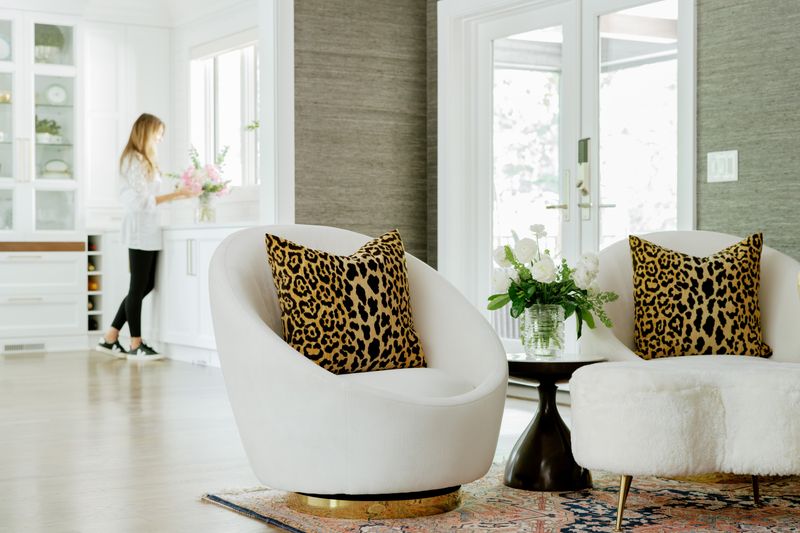 A sitting room in Des Moines with leopard print pillows on white swivel chairs against grasscloth walls.