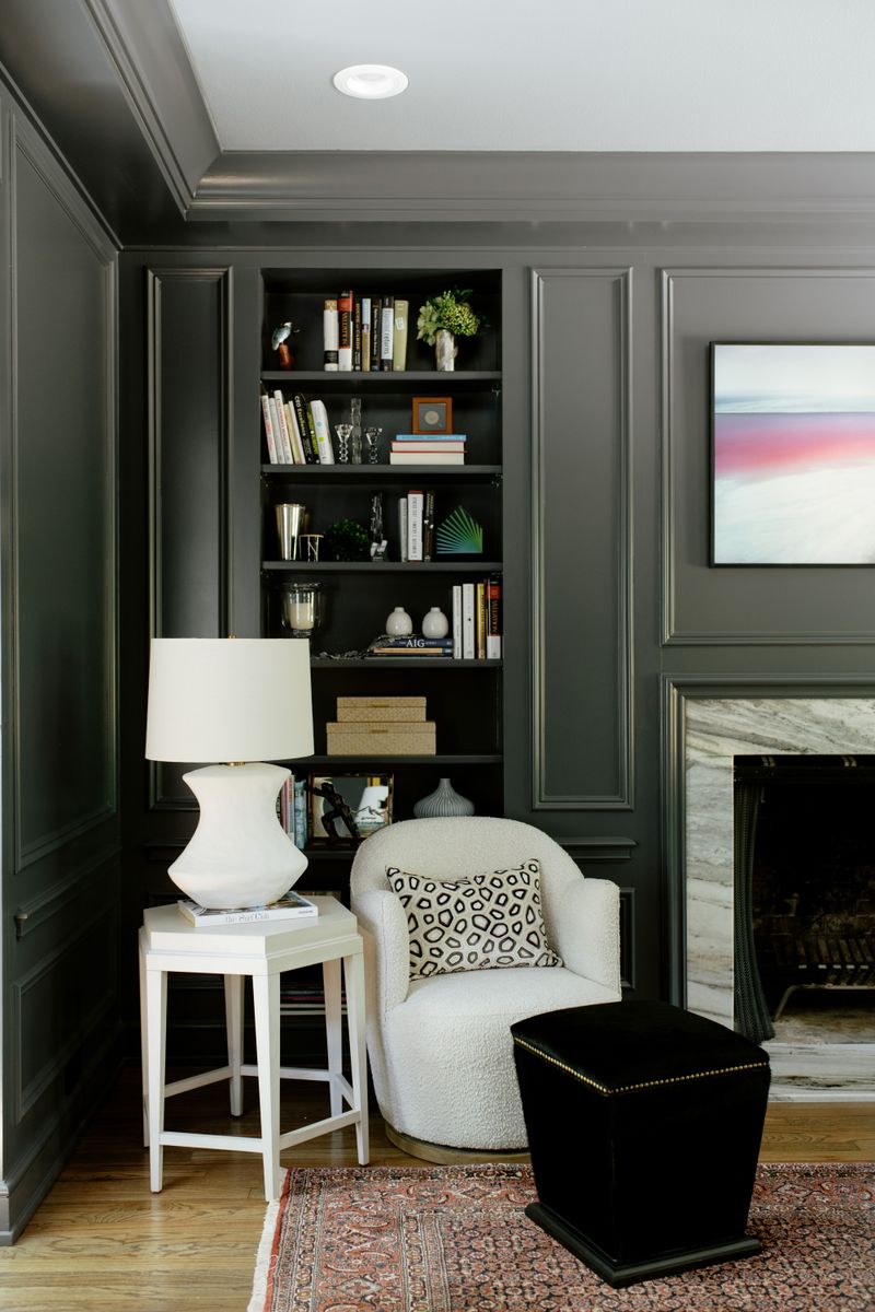 A study in Des Moines with dark green paneled walls and a built-in bookcase beside a marble fireplace.
