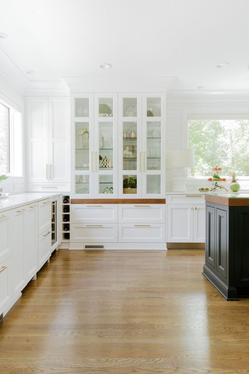 A white pantry in Des Moines with a glass front display cabinet over a walnut counter and brass pulls.