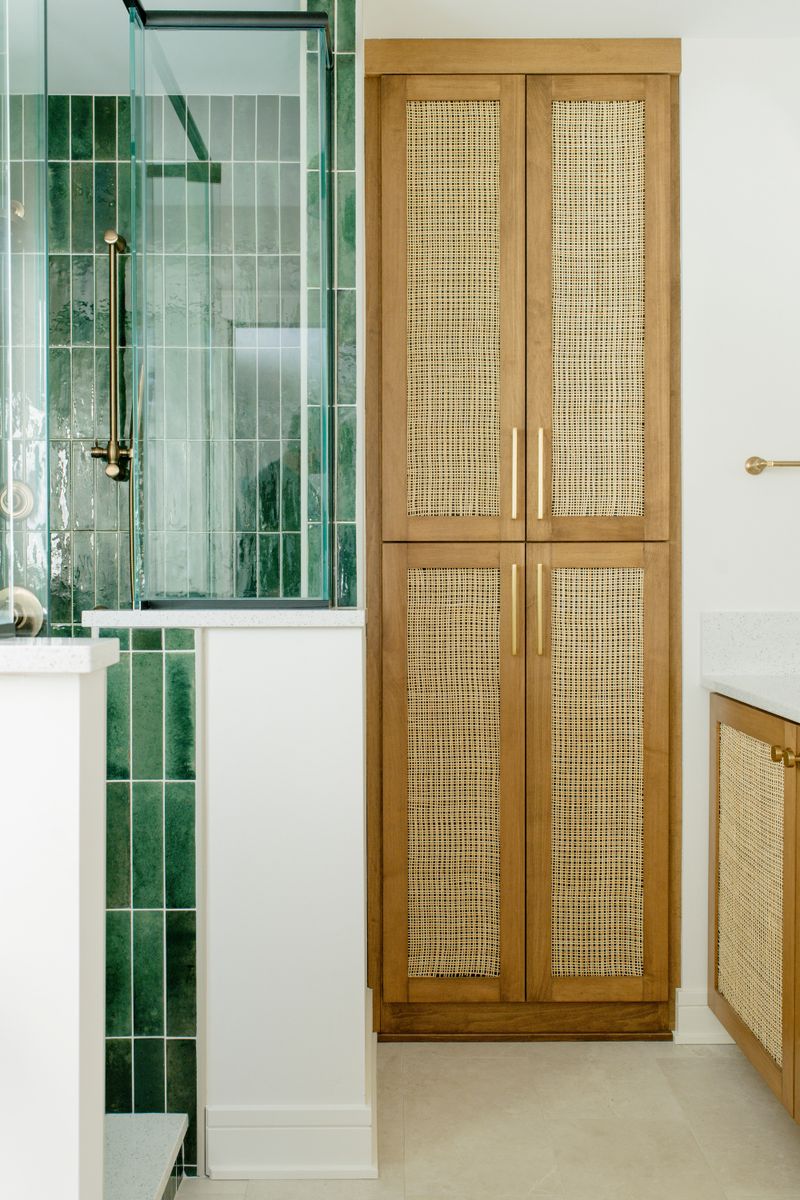 A bathroom in Des Moines with a cane and oak linen cabinet next to a green tiled shower.