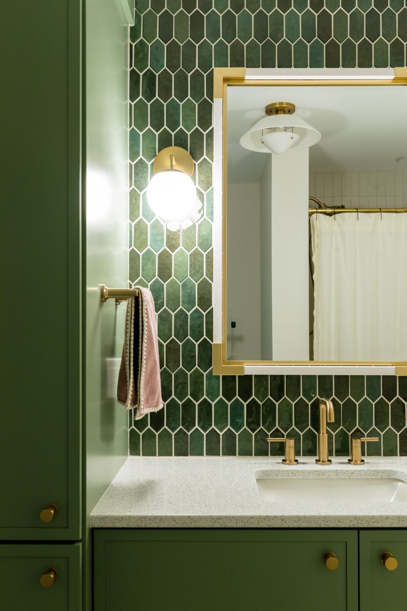 A bathroom in Des Moines with green picket tile behind a brass framed mirror and a terrazzo vanity top.