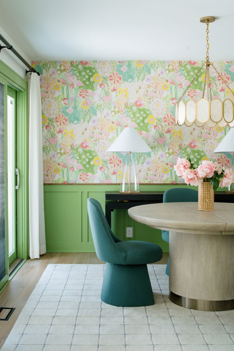 A dining room in Des Moines with floral wallpaper above green paneled wainscoting and teal swivel chairs.