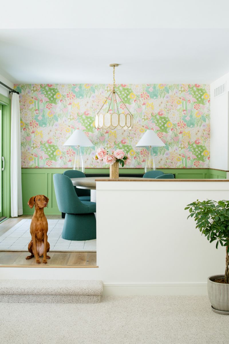 A dining room in Des Moines with floral wallpaper above green wainscoting and teal swivel chairs.