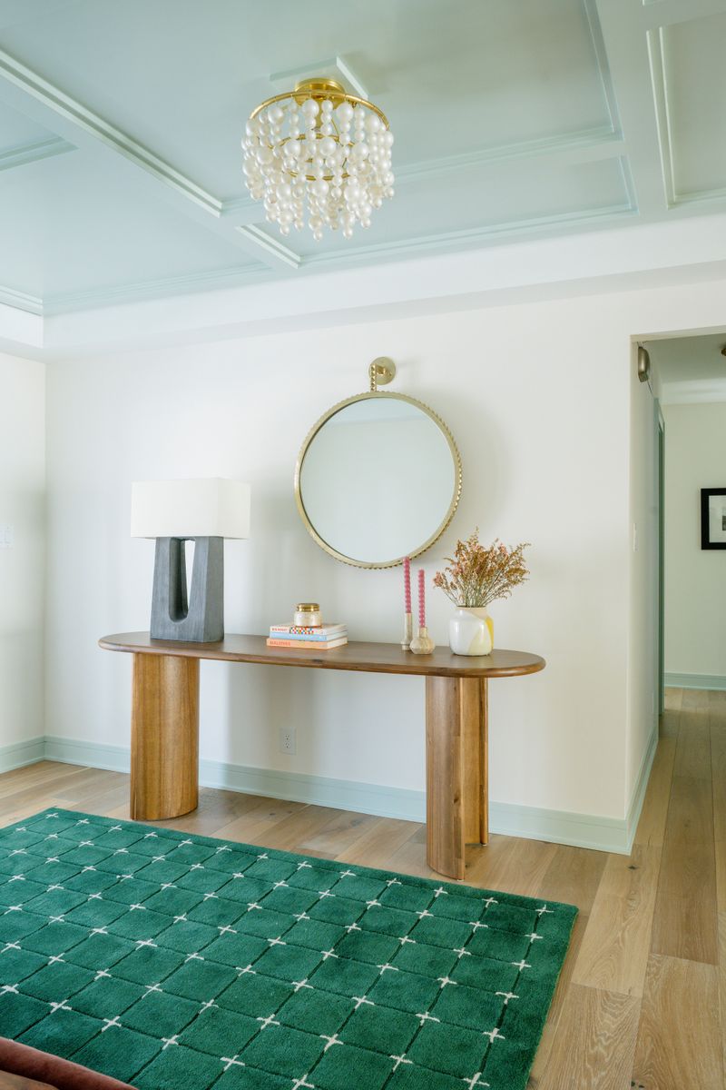 A Des Moines entry with a round brass mirror over a rounded wood console table and a green tile rug.
