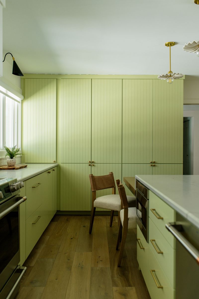 A green kitchen in Des Moines with floor to ceiling fluted cabinets and brass hardware over white oak floors.