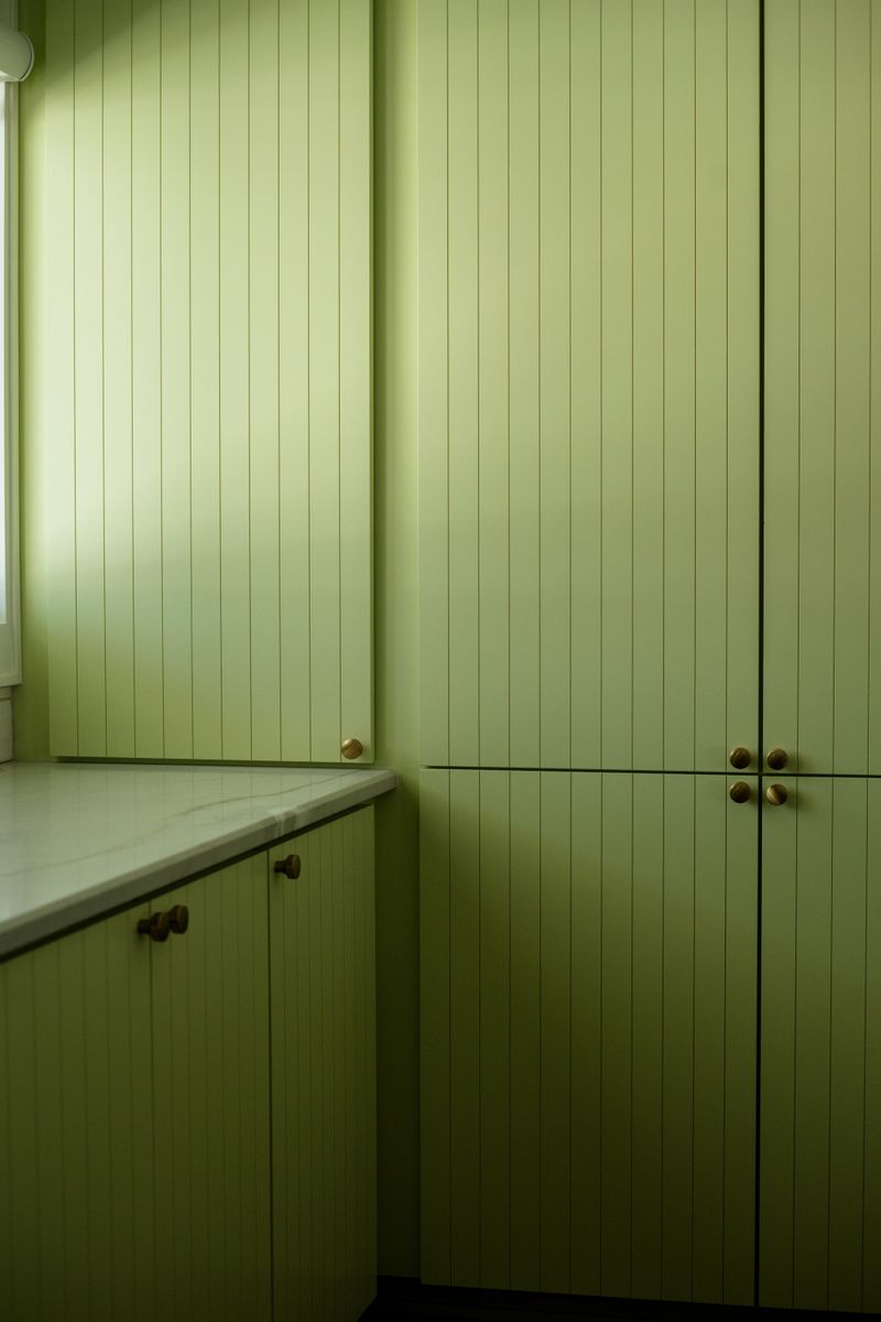 A green laundry room in Des Moines with brass knobs on beadboard cabinets and a marble counter.