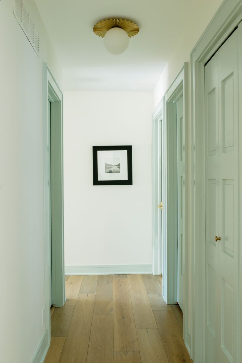 A white hallway in Des Moines with a pleated brass flush mount light over white oak floors.