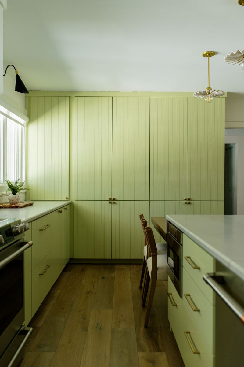 A Des Moines kitchen with a wall of green fluted cabinets and brass knobs, set over white oak floors.