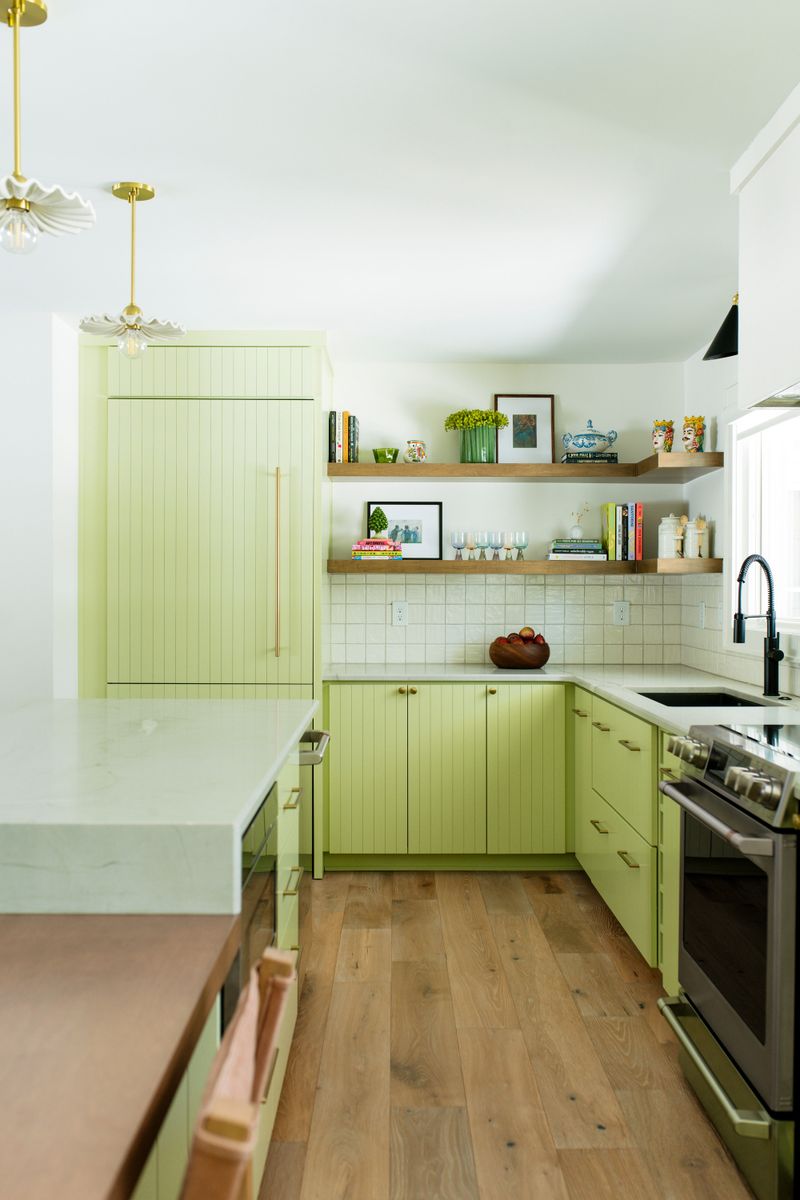 A Des Moines kitchen with green beadboard cabinets and open white oak shelves above a white tile backsplash.
