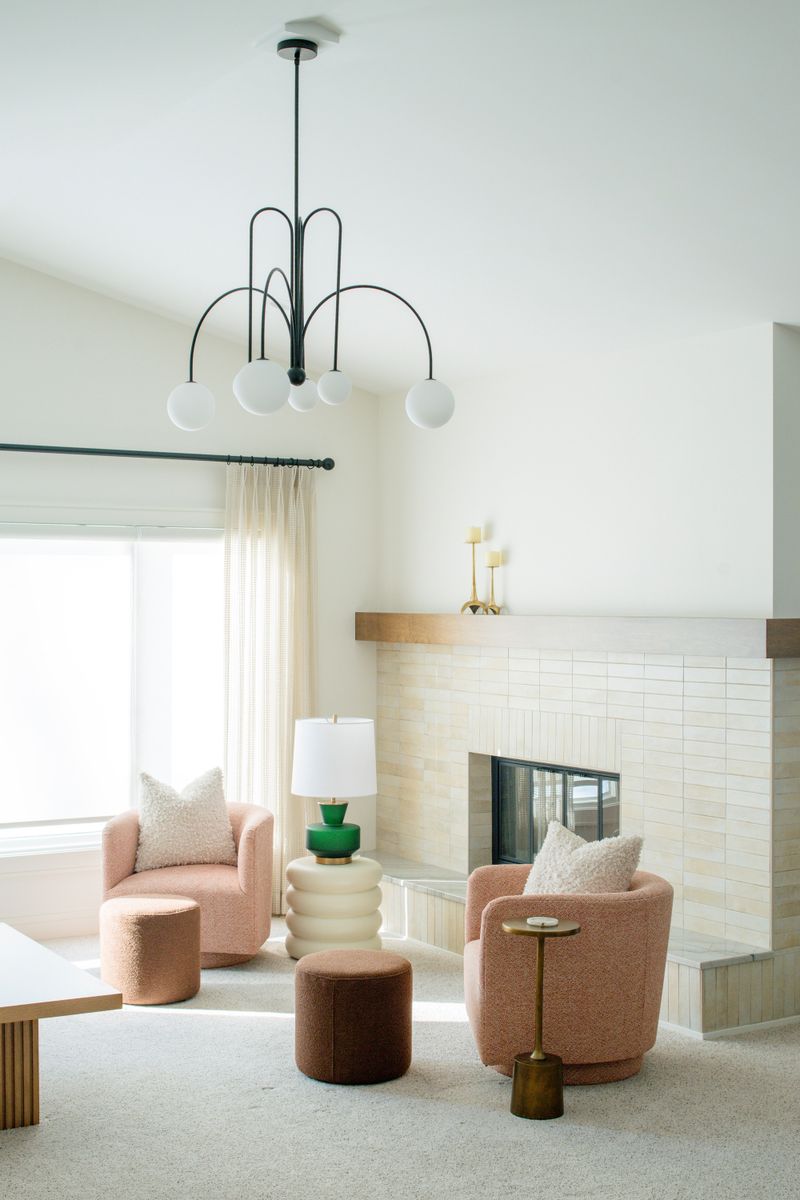 A living room in Des Moines with blush swivel chairs facing a cream stacked tile fireplace and wood mantel.