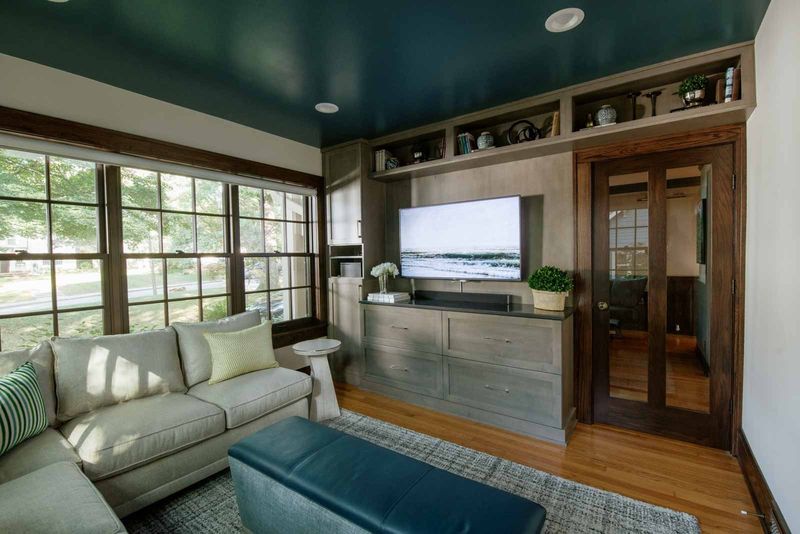 A living room in Des Moines with a deep teal ceiling above gray stained built-ins beside a glass pocket door.