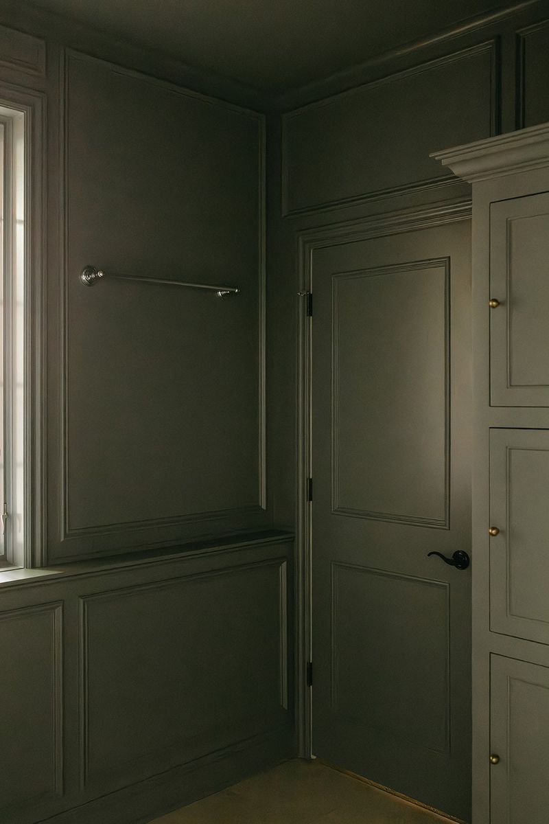 A dark olive green bathroom in Clive with paneled walls and a built-in cabinet with brass knobs.