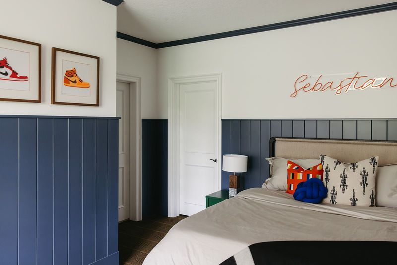 A kids bedroom in Clive with blue vertical board paneling below framed sneaker prints in walnut frames.