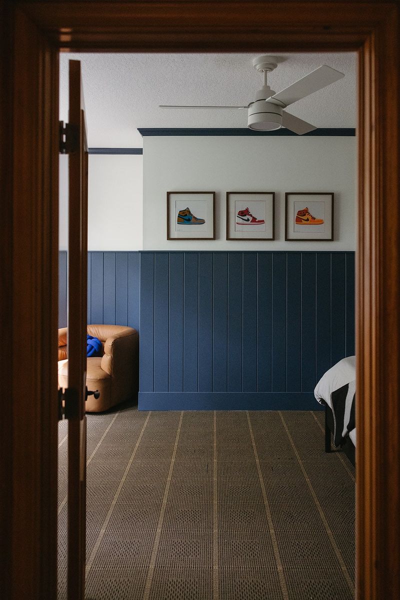 A kids bedroom in Clive with navy vertical board wall paneling and framed sneaker prints above it.