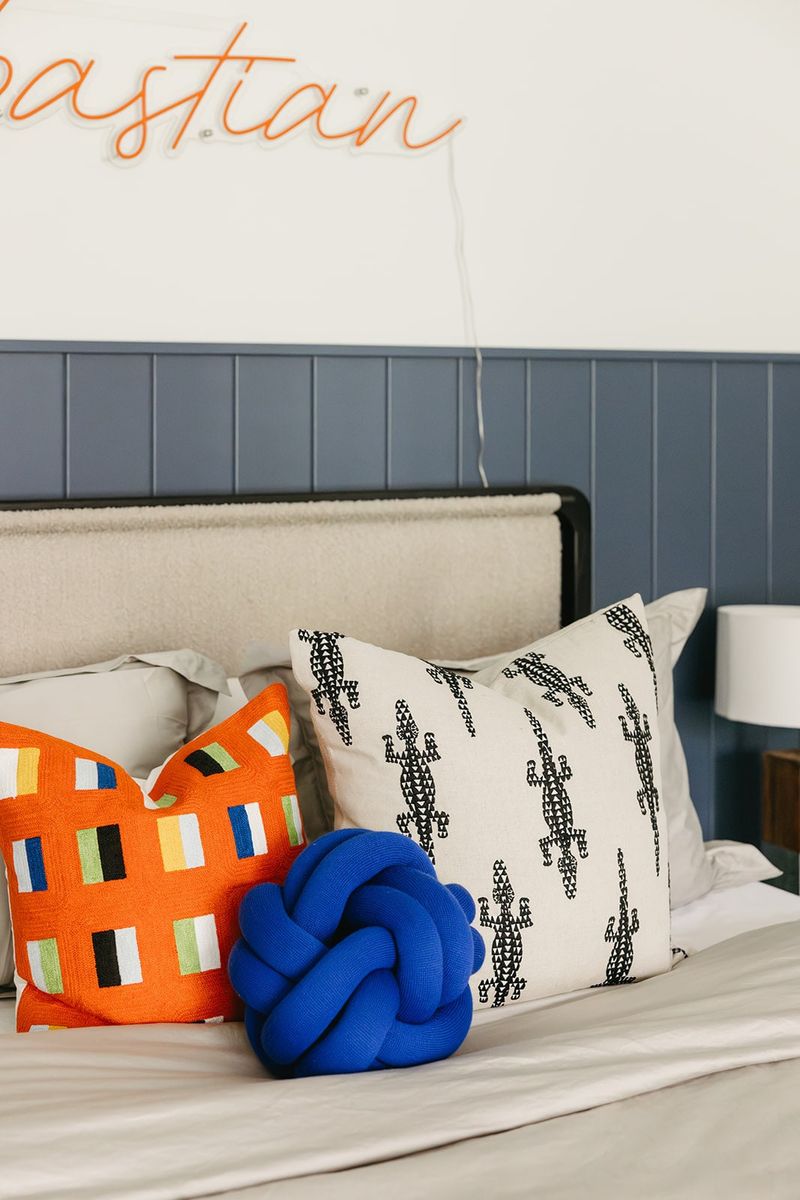 A kids bedroom in Clive with navy vertical wall paneling behind a cream upholstered bed and bright orange pillow.