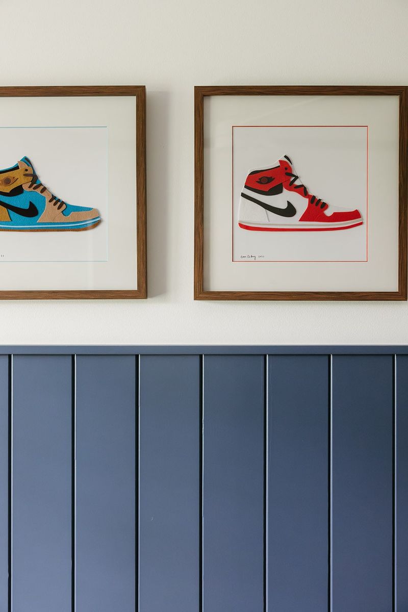 Framed sneaker art in walnut frames above blue vertical board wainscoting in a Clive bedroom.