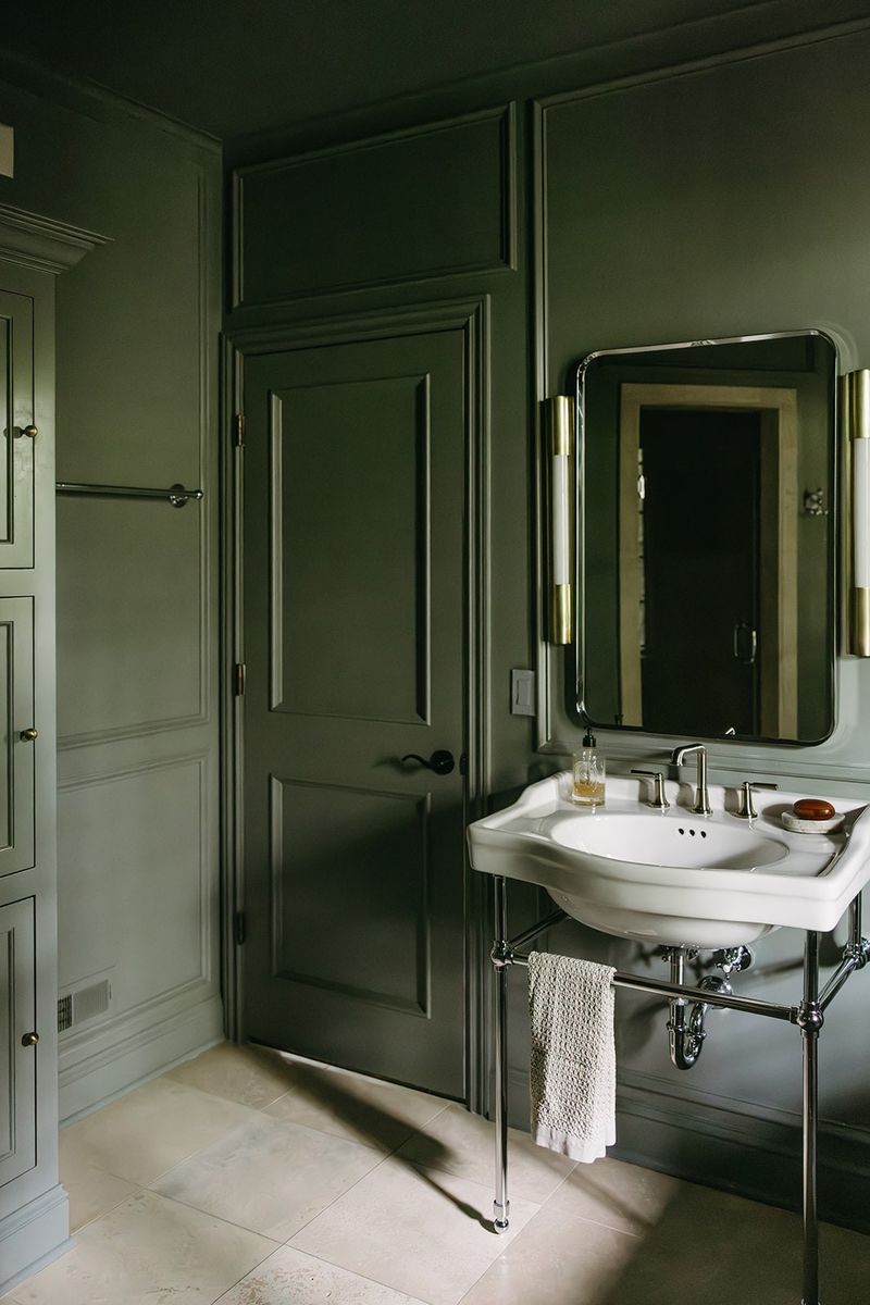 A green bath in Clive with a white console sink on polished chrome legs over pale stone tile floors.