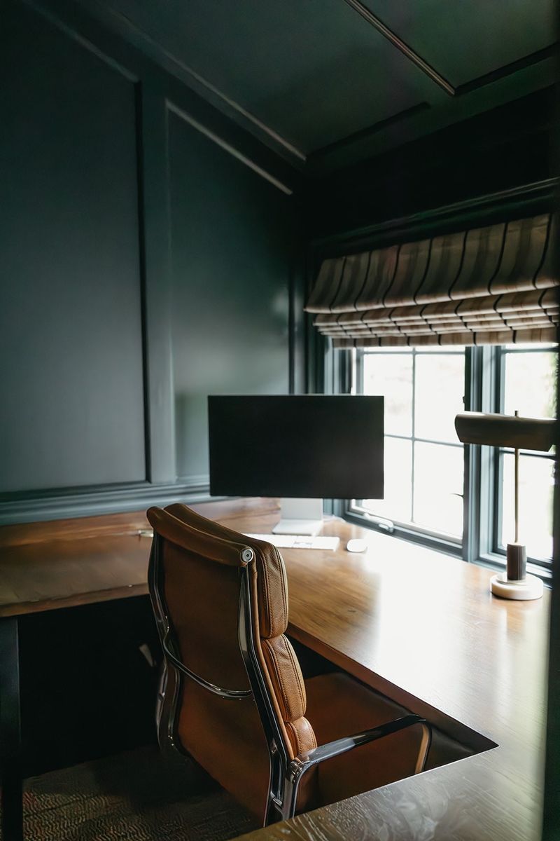 A dark green home office in Clive with a tan leather desk chair pulled up to a warm wood desk.