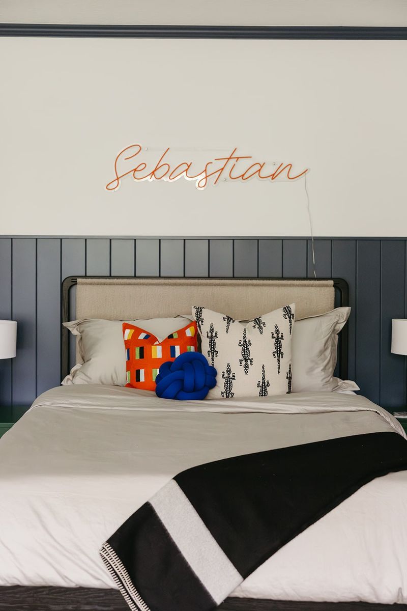 A kids bedroom in Clive with navy vertical shiplap paneling behind a linen headboard and a bright blue knot pillow.