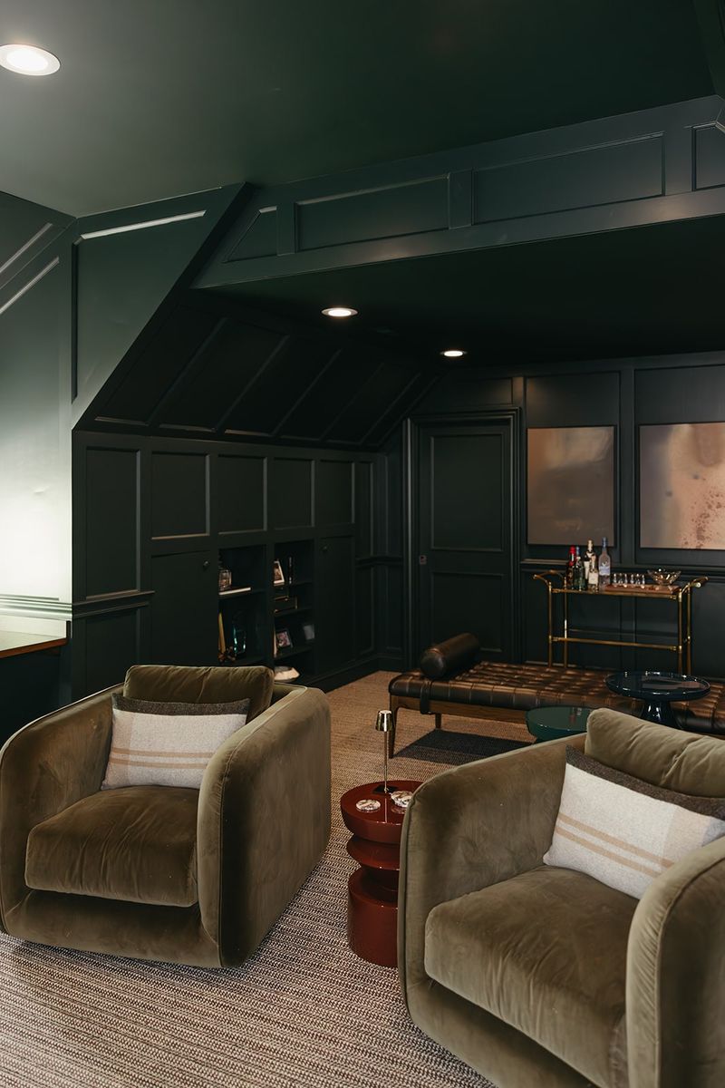 A dark green paneled lounge in Clive with olive velvet swivel chairs around a red side table.