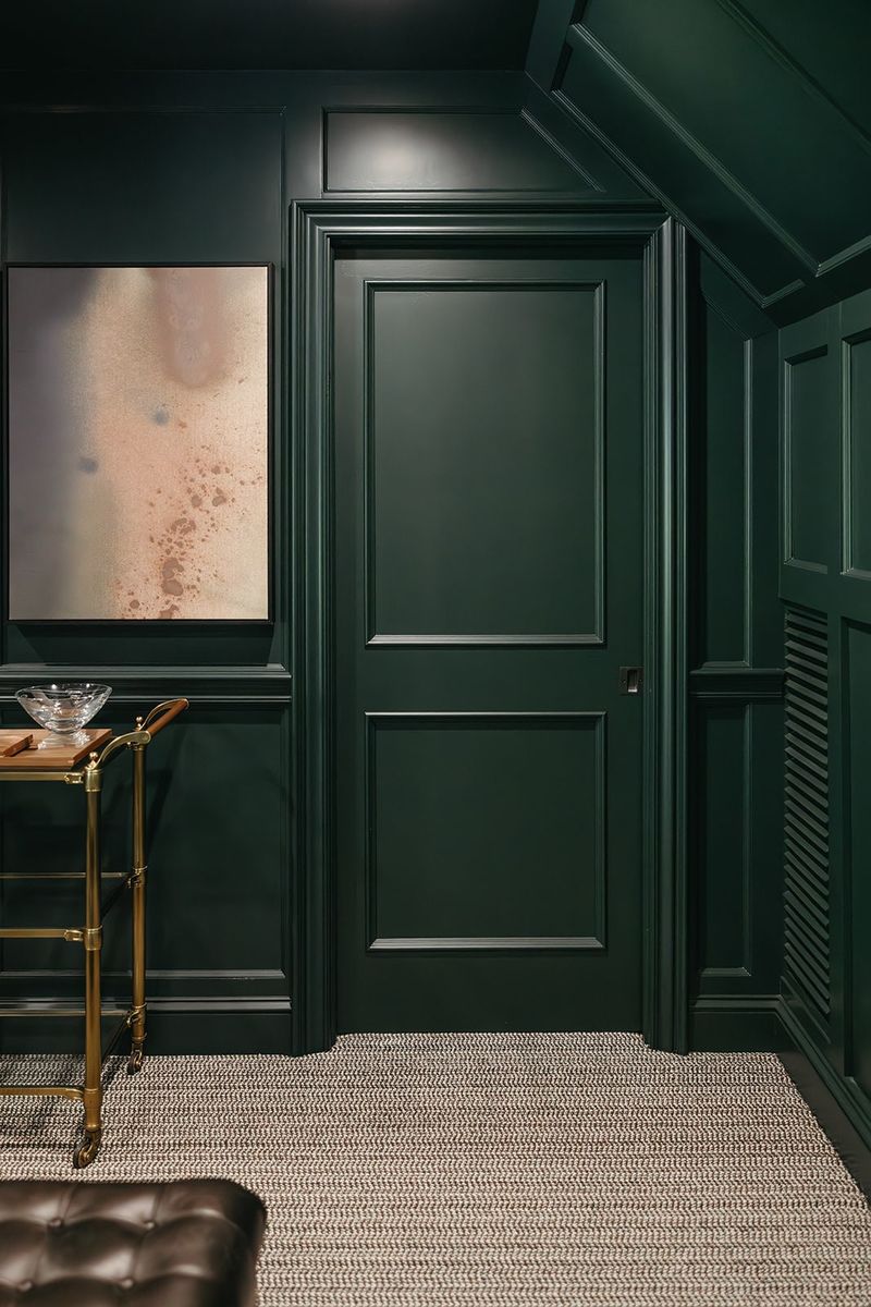 A dark green media room in Clive with paneled millwork wrapping the door and a brass bar cart beside it.