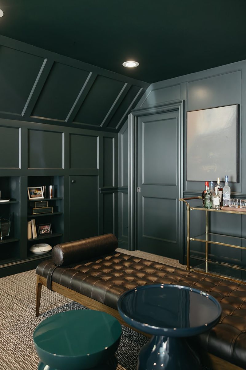 A dark green paneled home office in Clive with a tufted brown leather daybed and a brass bar cart.