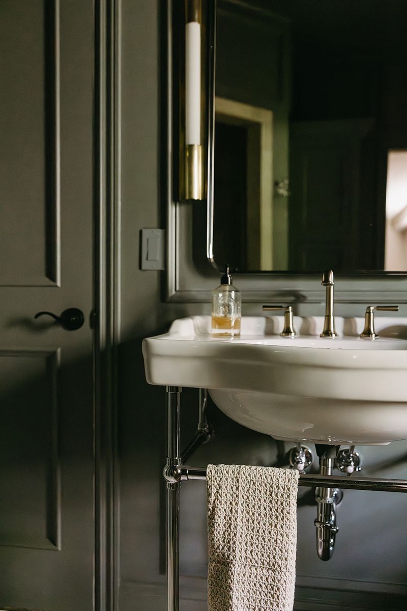 A dark green powder room in Clive with a white console sink on a polished chrome stand.