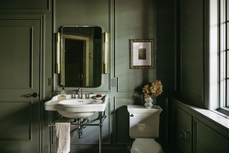 A powder room in Clive with dark green paneled walls and a gold framed print above the toilet.