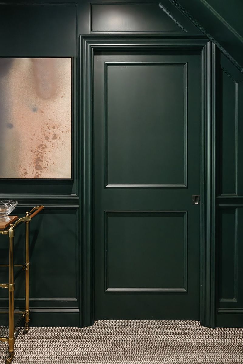 A study in Clive painted dark green from wall panels to door, with a brass bar cart in the corner.