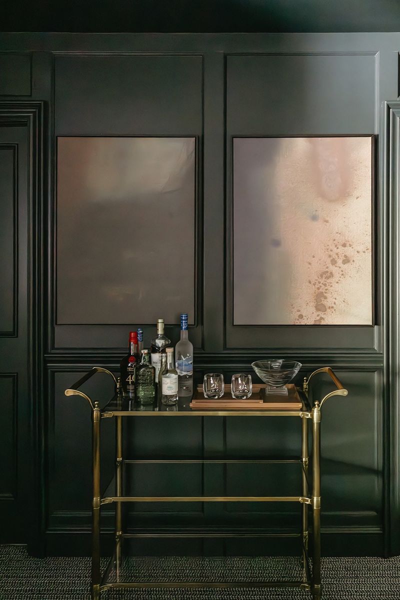 A wet bar in Clive with a brass bar cart against a wall of glossy dark green panel moulding.