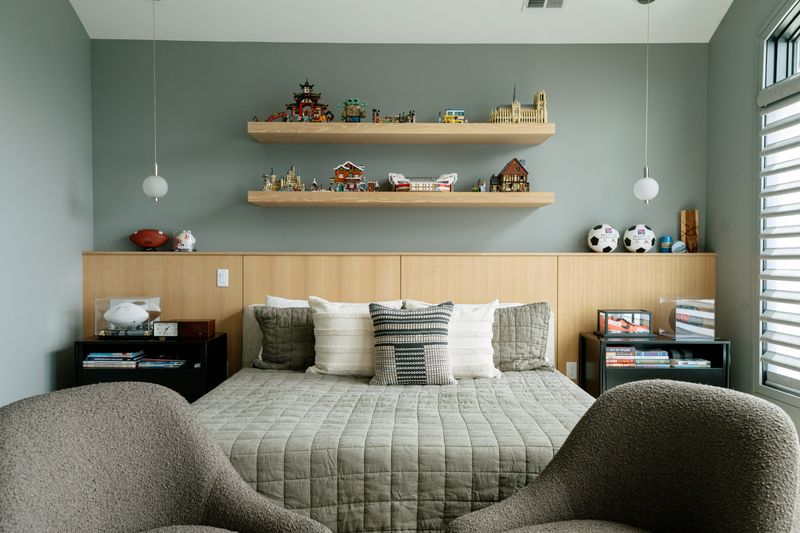 A boy's bedroom in West Des Moines with a full width white oak headboard wall against sage green paint.
