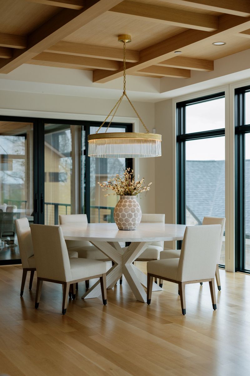 A dining room in West Des Moines with a brass and glass chandelier over a round white oak table.