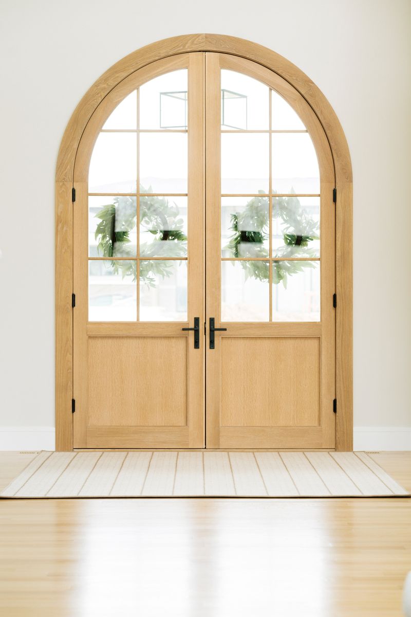 An arched white oak double entry door in West Des Moines with black hardware and greenery wreaths.